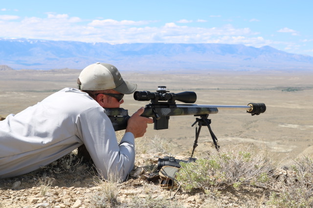 Prone with a scoped custom bolt rifle in high desert.